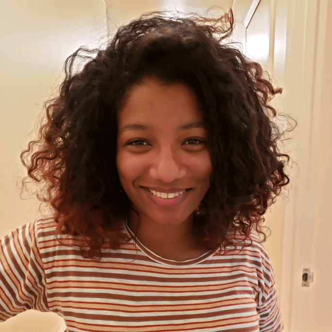 woman with brown hair and striped shirt smiling and standing in a white room