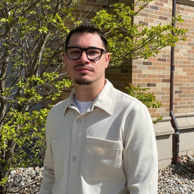 man with black hair in black rimmed glasses with goatee and light colored shirt standing outside