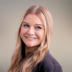 smiling woman with long blonde hair and wearing a black suit jacket standing against a gradient background